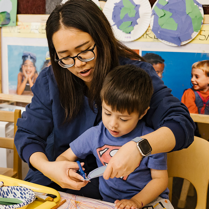 teacher helping young child cut with scissors