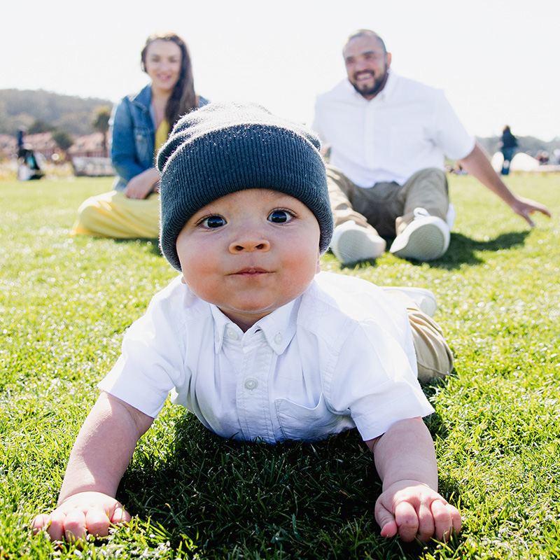 baby crawling toward camera outside with parents in background