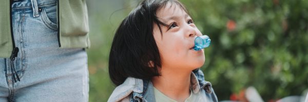 close up on young girl outside blowing a blue whistle